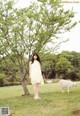 A woman in a yellow dress standing next to a tree.