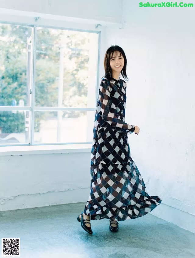 A woman in a long dress standing in front of a window.