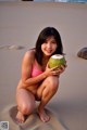 A woman in a pink bikini holding a coconut on the beach.