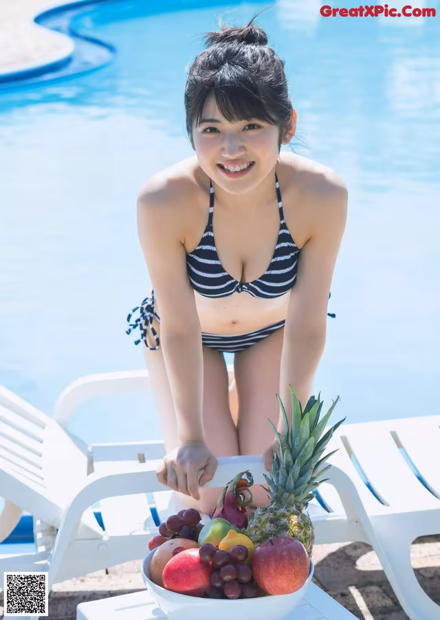 A woman in a bikini holding a bowl of fruit by a pool.