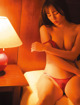 A woman in a red lingerie sitting on a bed next to a lamp.