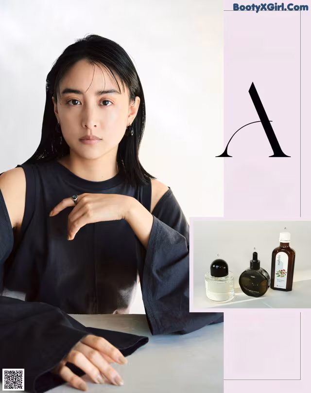 A woman sitting at a table with a bottle of perfume.