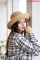 A woman wearing a straw hat leaning against a wall.