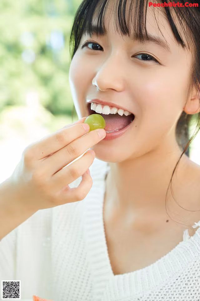 A woman eating a piece of fruit with her mouth open.
