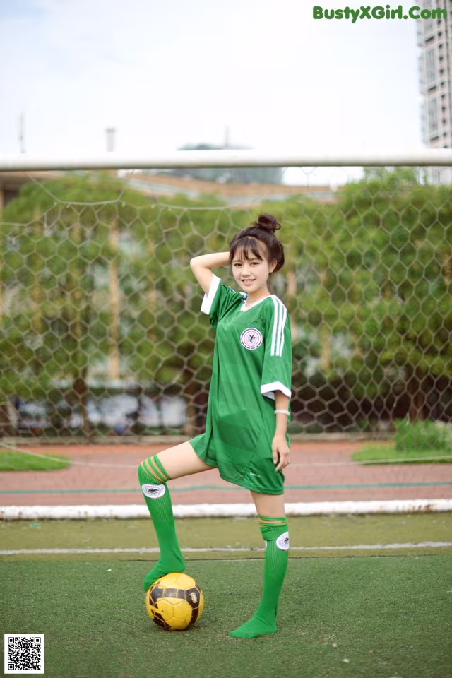 A woman in a green soccer uniform posing with a soccer ball.