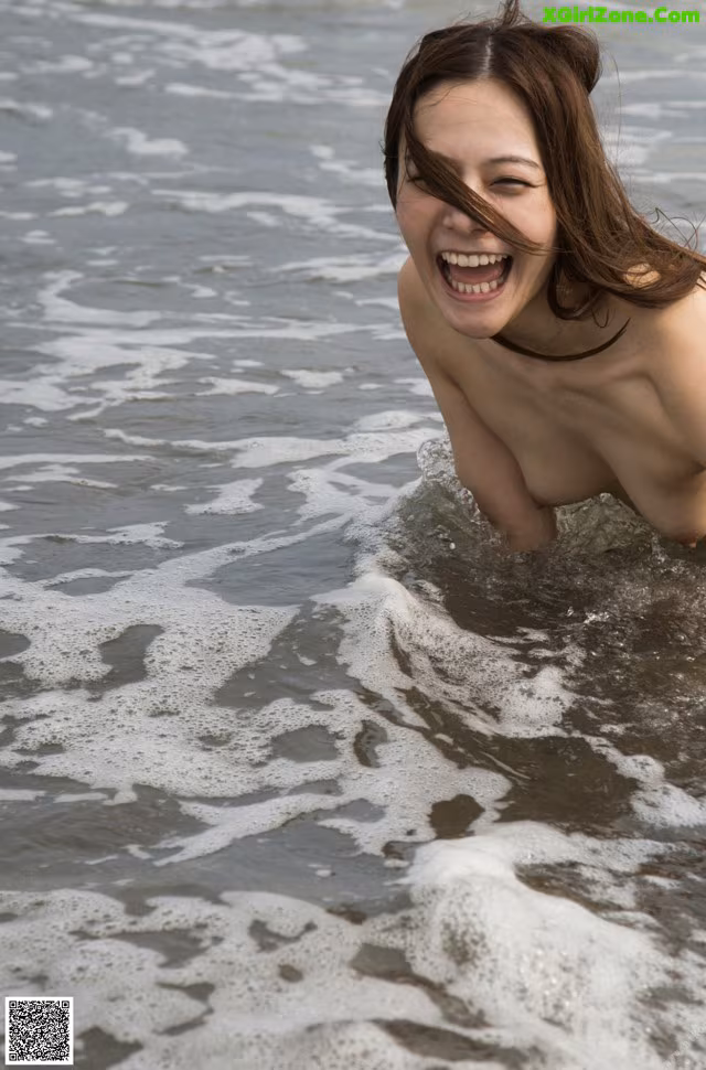 A naked woman in the ocean with her mouth open.