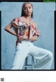 A woman sitting on a stool wearing white pants and a colorful top.