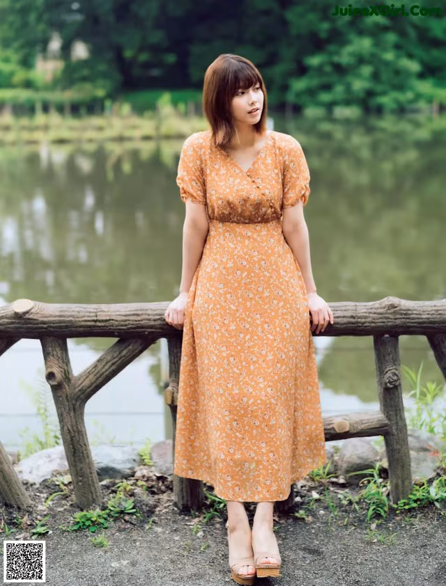 A woman standing on a wooden bridge near a lake.